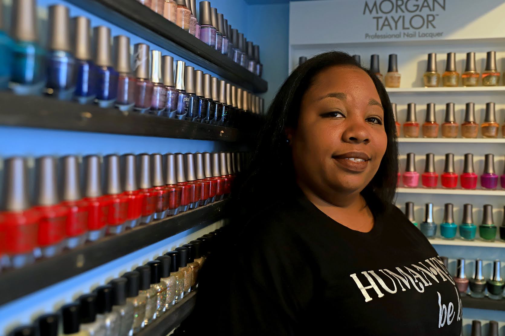 A Black woman stands in front of a row of nail polish colors.