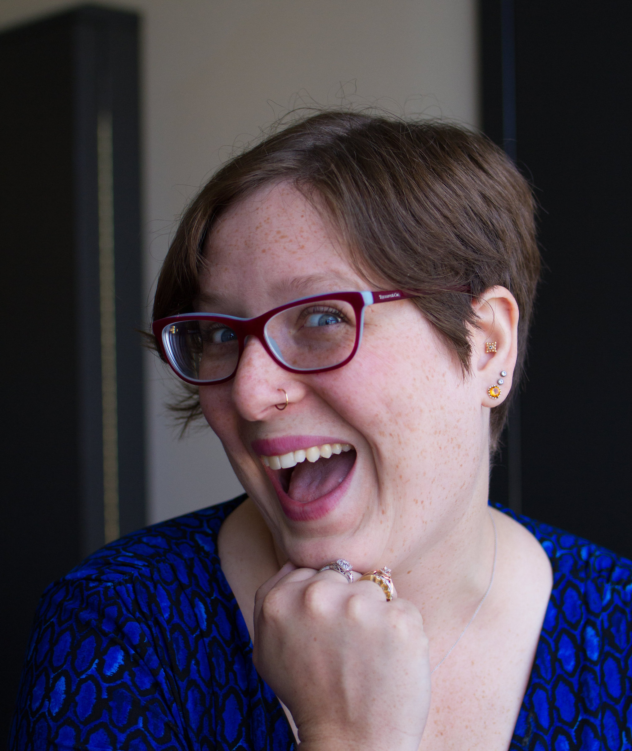 Photograph of a white woman with short hair smiling at the camera. She’s making a silly face and resting her head on her hand.